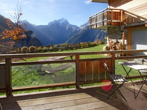 Une terrasse en bois offrant une vue sur un paysage montagneux, un mur de pierres et une pile de bois de chauffage.