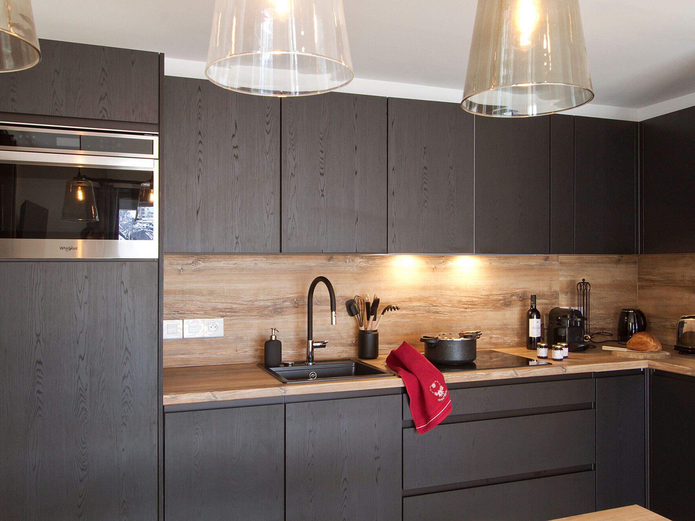 Cocina moderna con gabinetes de madera oscura, extractor de acero inoxidable, pileta doble e iluminación colgante.
