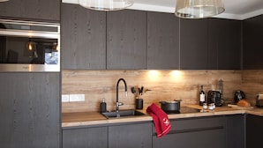 Une cuisine moderne avec des meubles de couleur bois foncé, une hotte en acier inoxydable, un évier double et des luminaires suspendus.