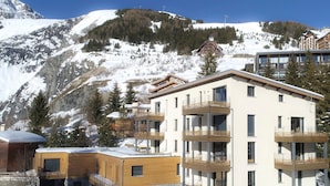 Un hôtel moderne à plusieurs étages, doté de balcons, qui se dresse sur fond de montagnes enneigées.