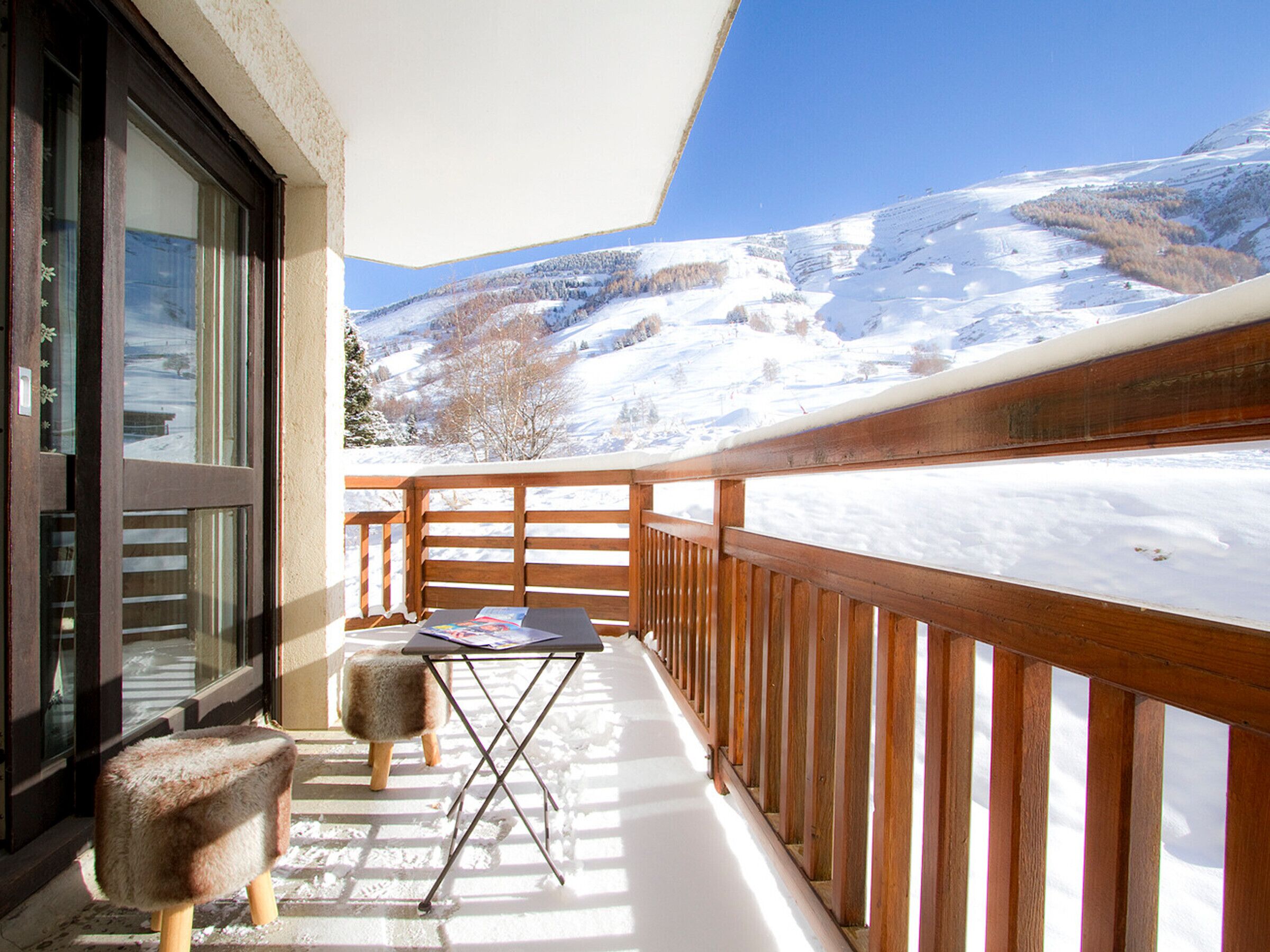 A balcony with a wooden railing, a small table, and two stools.