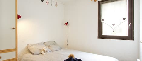 A bedroom with a bed, a window, a lamp, and a small stool.