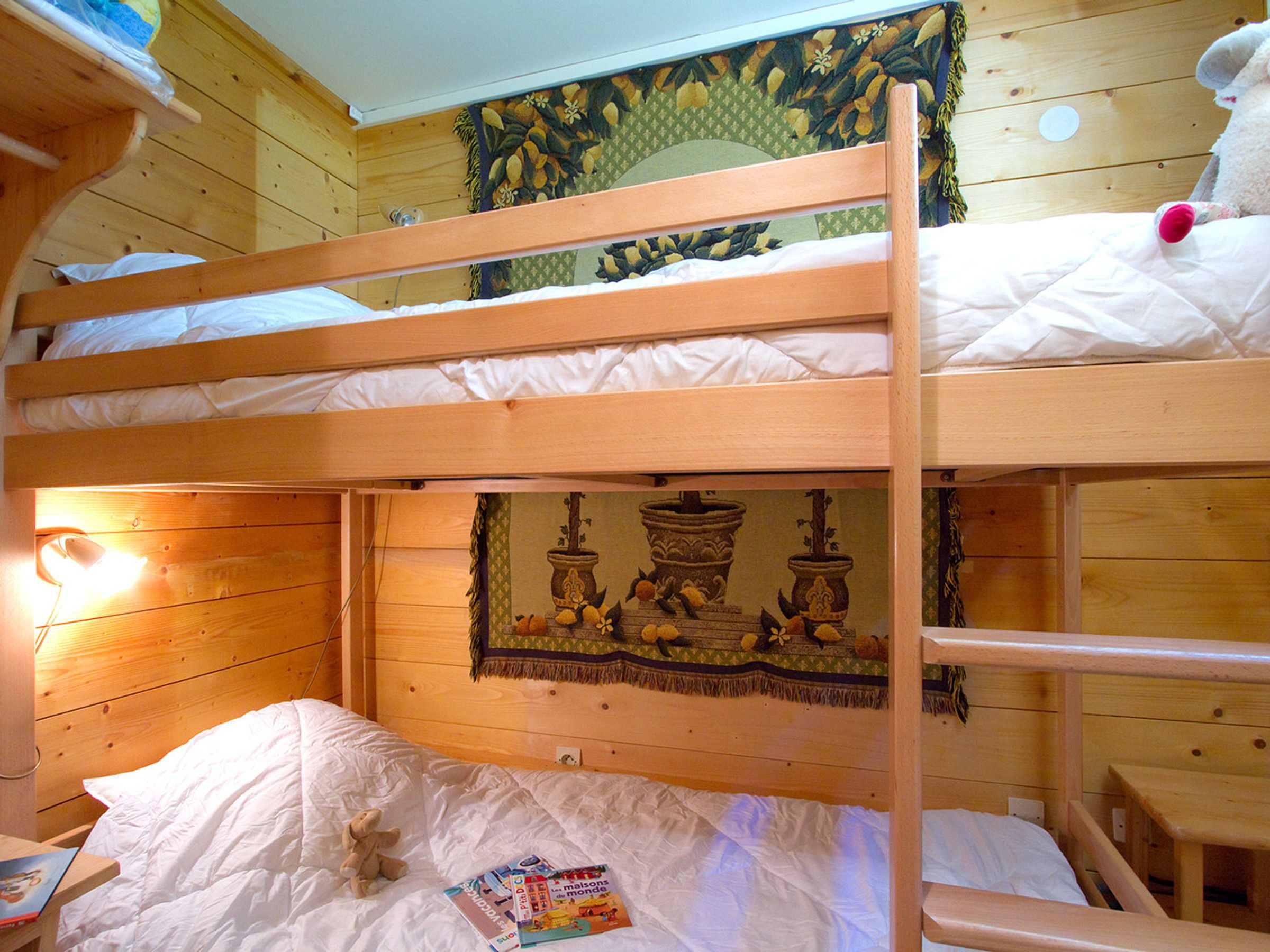 Een slaapkamer met een stapelbed, een houten hoofdbord, wandtapijt en een kleine tafel met een lamp.