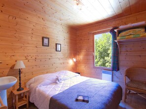 Een houten kamer met een bed, een stoel, een raam met gordijnen en een wastafel.