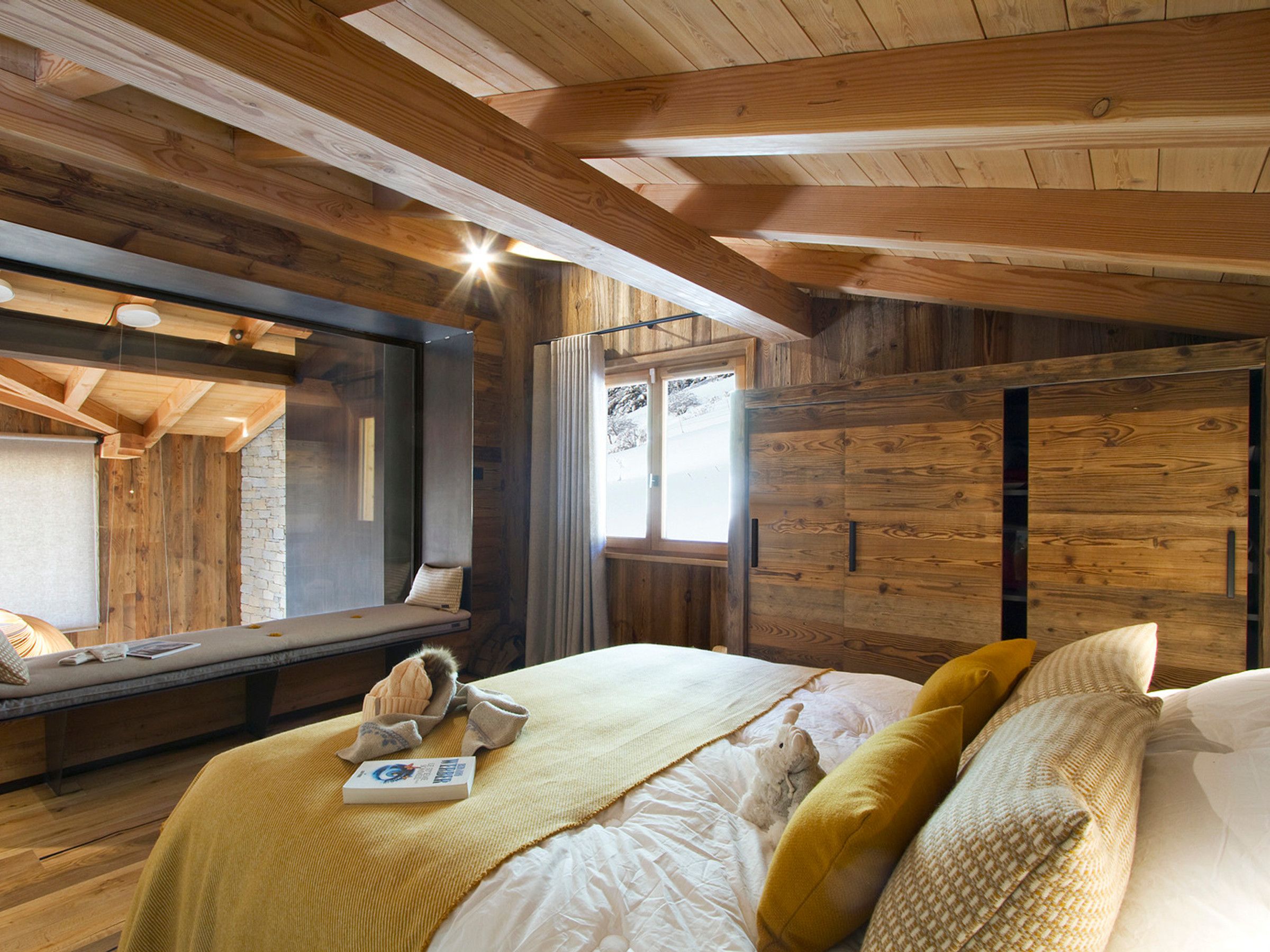Une chambre confortable avec un plafond en bois, un lit avec des oreillers, une fenêtre et un banc avec un coussin.