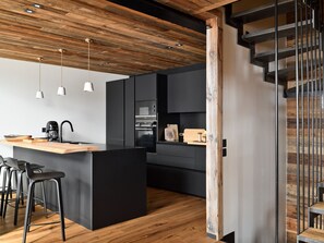 Eine moderne Küche mit Holzbalkendecke, schwarzen Schränken und einer zentralen Kochinsel mit Barhocker.