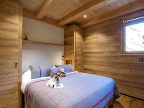Ein Holzblockhaus-Interieur mit einem Bett, Kissen, einem Teddybären und einem Fenster.