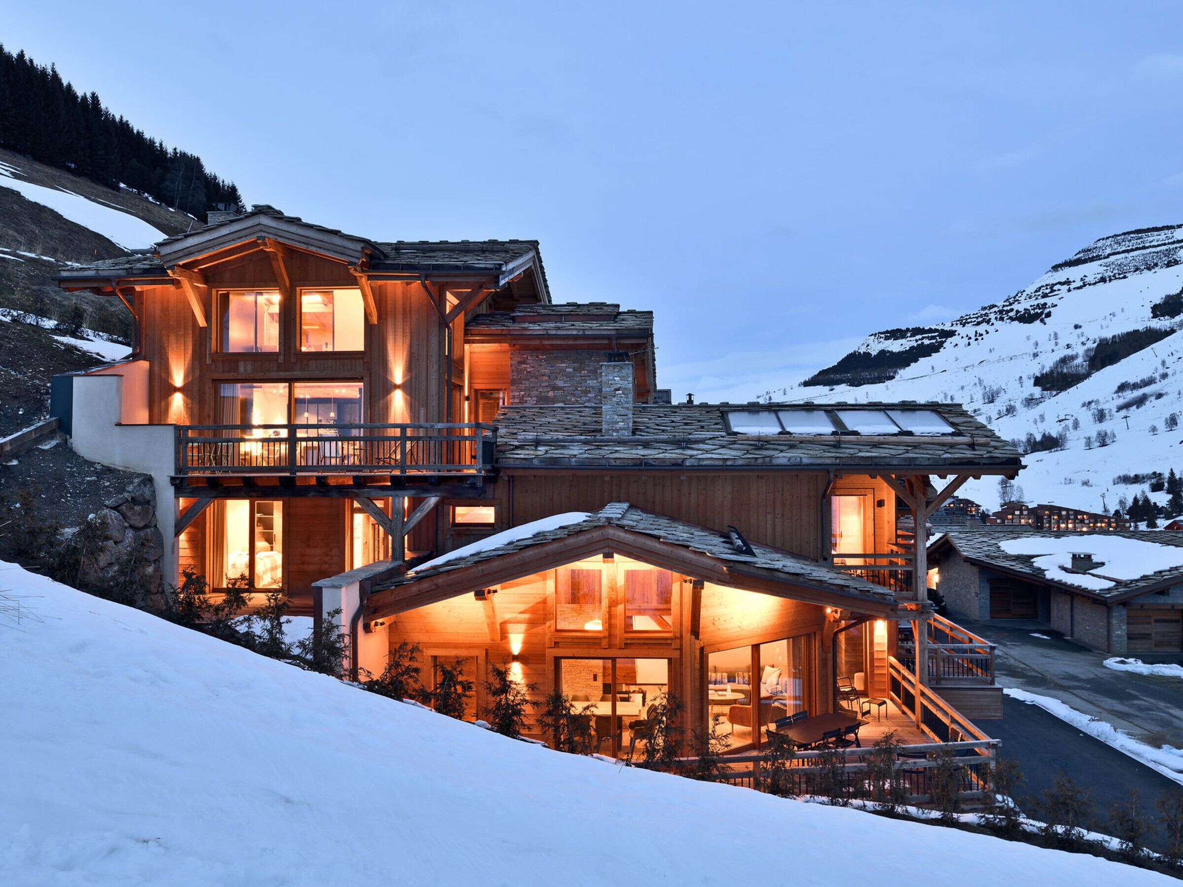 Un chalet en bois à plusieurs niveaux, doté de balcons, d’un coin repas et offrant une vue sur une montagne enneigée.