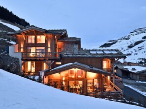 Eine mehrstöckige Holzhütte mit Balkonen, einem Essbereich und Blick auf einen verschneiten Berg.