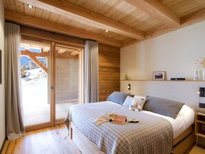 Ein Schlafzimmer mit einem großen Bett, einer Holzbalkendecke, einer Schiebetür zu einem Balkon und einem Nachttisch mit Lampe.