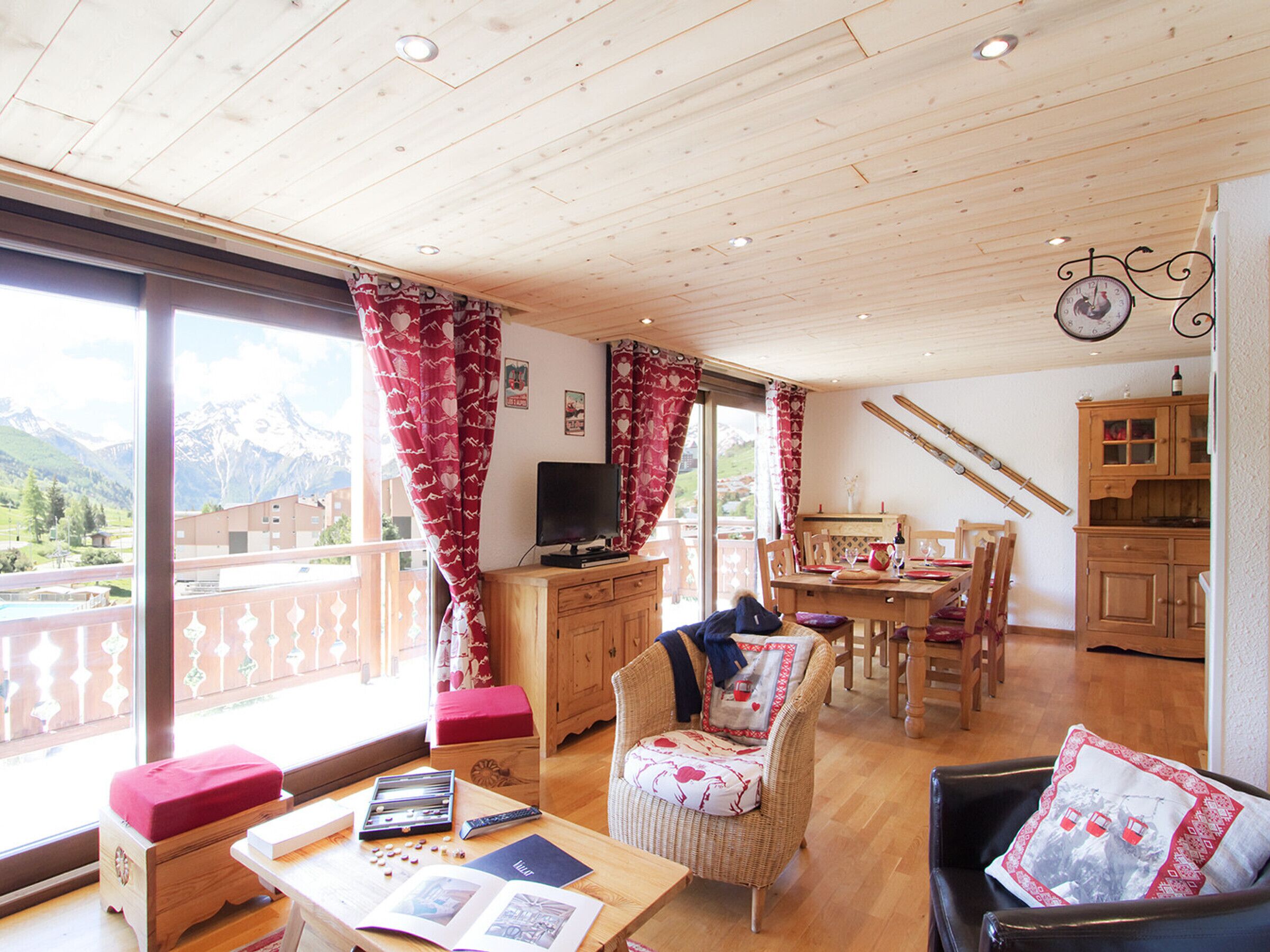 Une pièce dotée d’un plafond en bois, d’un téléviseur, d’un coin repas avec des chaises et une table, et offrant une vue sur les montagnes grâce à de grandes fenêtres.