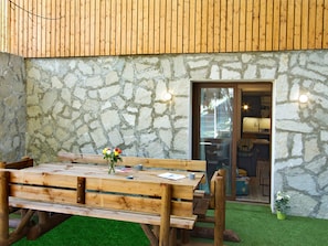 A wooden table with benches and a vase of flowers in front of a stone wall with a glass door leading to a kitchen area. - Apartment with terrace - 4 guests (Les Deux Alpes)