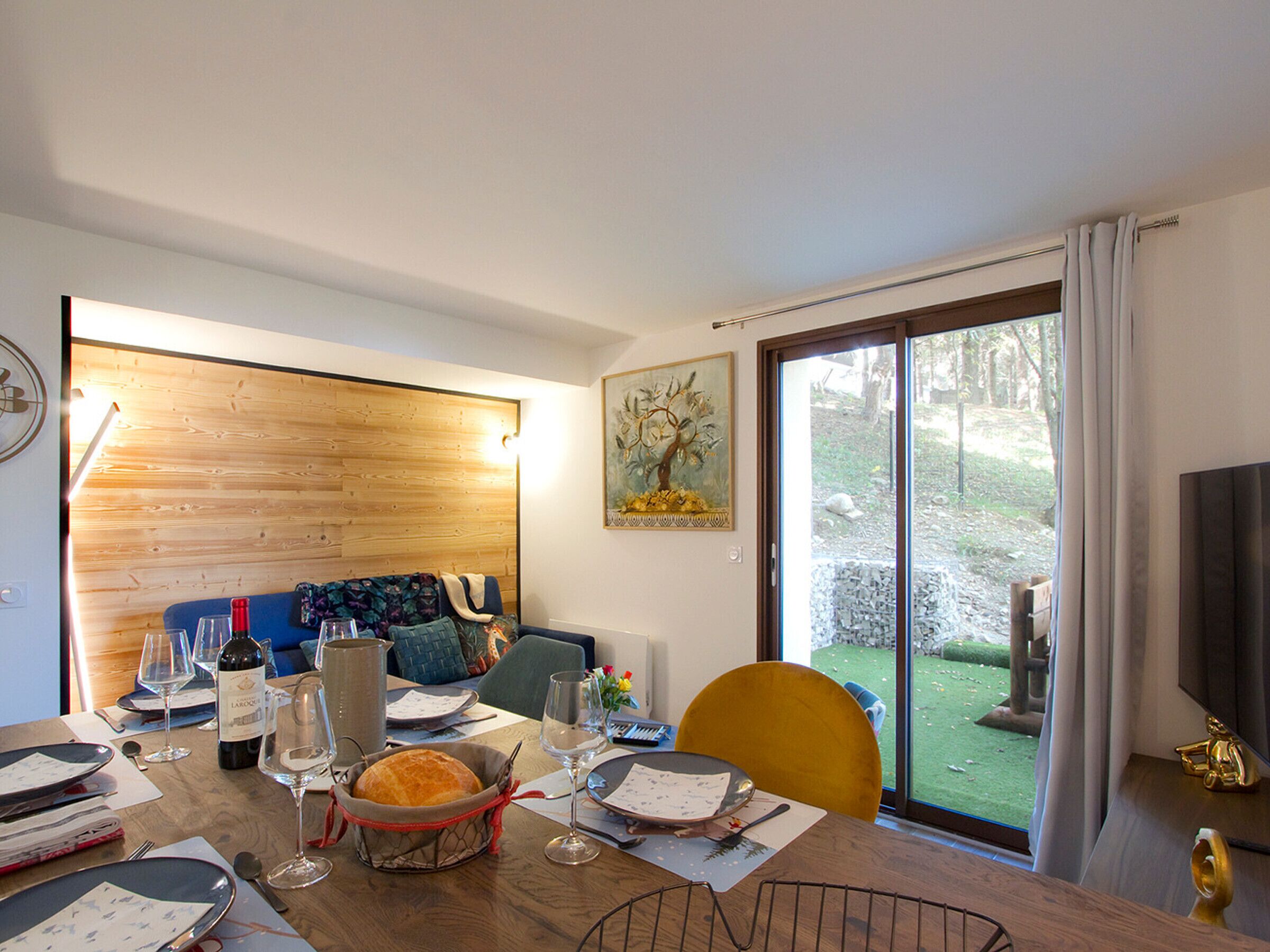 Un coin repas avec une table en bois mise pour le repas, un canapé et un tableau accroché au mur.