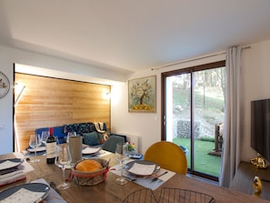 A dining area with a wooden table set for a meal, a sofa, and a painting on the wall. - Apartment with terrace - 4 guests (Les Deux Alpes)