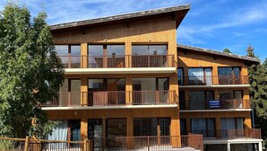 Un edificio de madera de varios pisos, con balcones, una zona de estacionamiento y un letrero que anuncia una venta.
