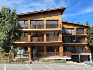 A multi-story wooden building with balconies, a parking area, and a sign indicating a sale. - Apartment with terrace - 4 guests (Les Deux Alpes)