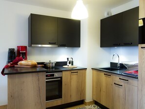 A compact kitchen with wooden cabinets, a built-in oven, a coffee maker, and a bread loaf on the counter. - Charming apartment in the heart of Les Deux Alpes (Les Deux Alpes)