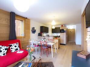 Ein gemütlicher, kleiner Wohnraum mit einem roten Sofa, einem Esstisch mit Stühlen, einer Küchenzeile und einem Fernseher.