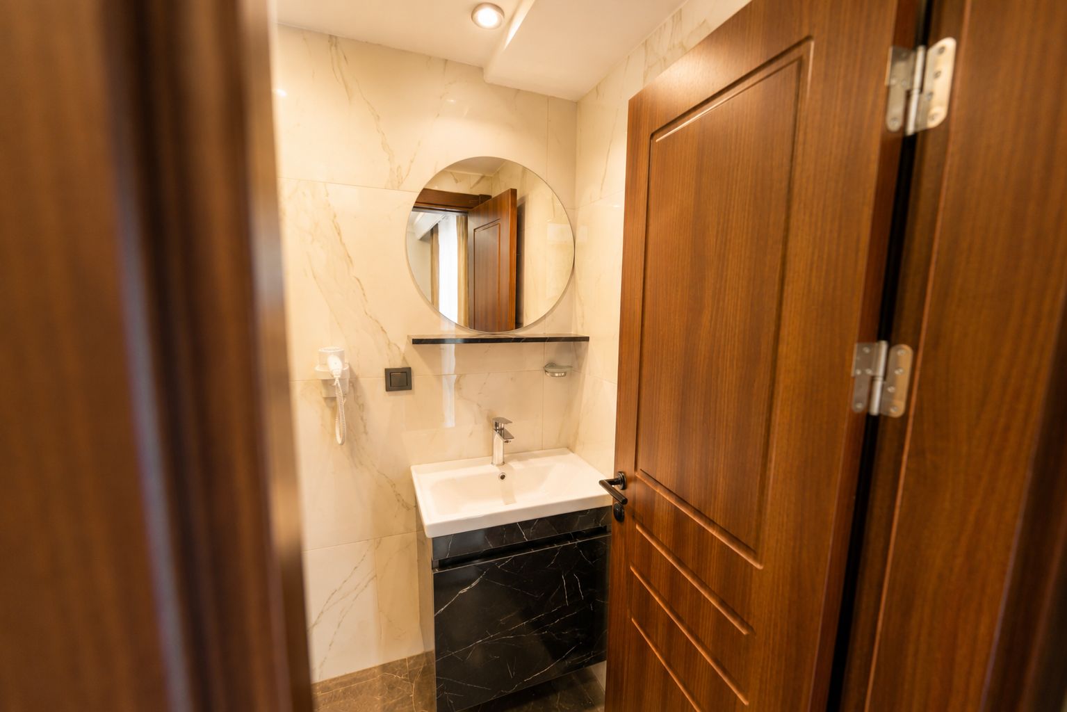 Ein Badezimmer mit Holztür, Waschbecken und einem Spiegel darüber.