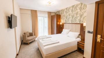 Une chambre d’hôtel avec un lit, une chaise, un téléviseur et un mur orné d’un motif de feuilles.