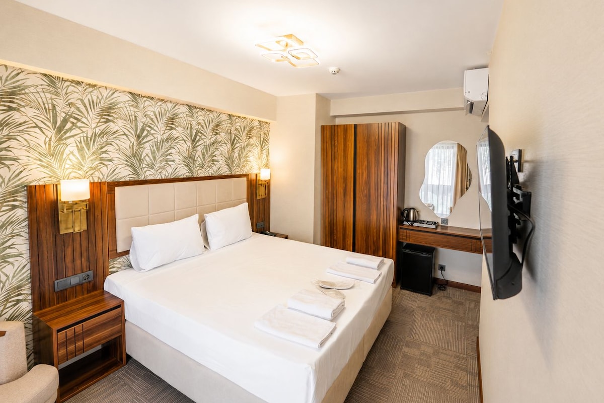 Habitación de hotel con una cama grande, cabecero de madera, un escritorio con espejo y un televisor en la pared.