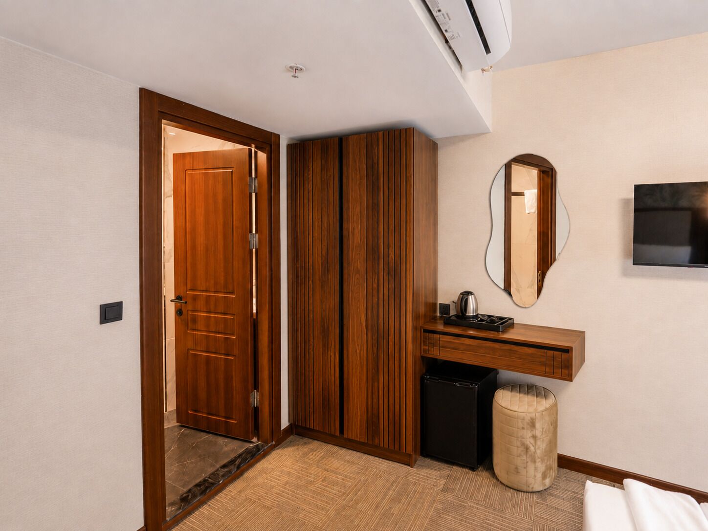 A hotel room with a wooden wardrobe, a small kitchenette, a mirror, and a television.
