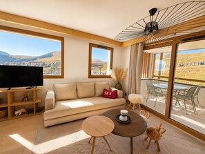 Ein modernes Wohnzimmer mit Sofa, Couchtisch, Fernseher und Blick ins Freie.