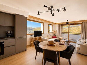 Ein moderner Wohnraum mit Küche, Essbereich und Sitzgelegenheiten an großen Fenstern.