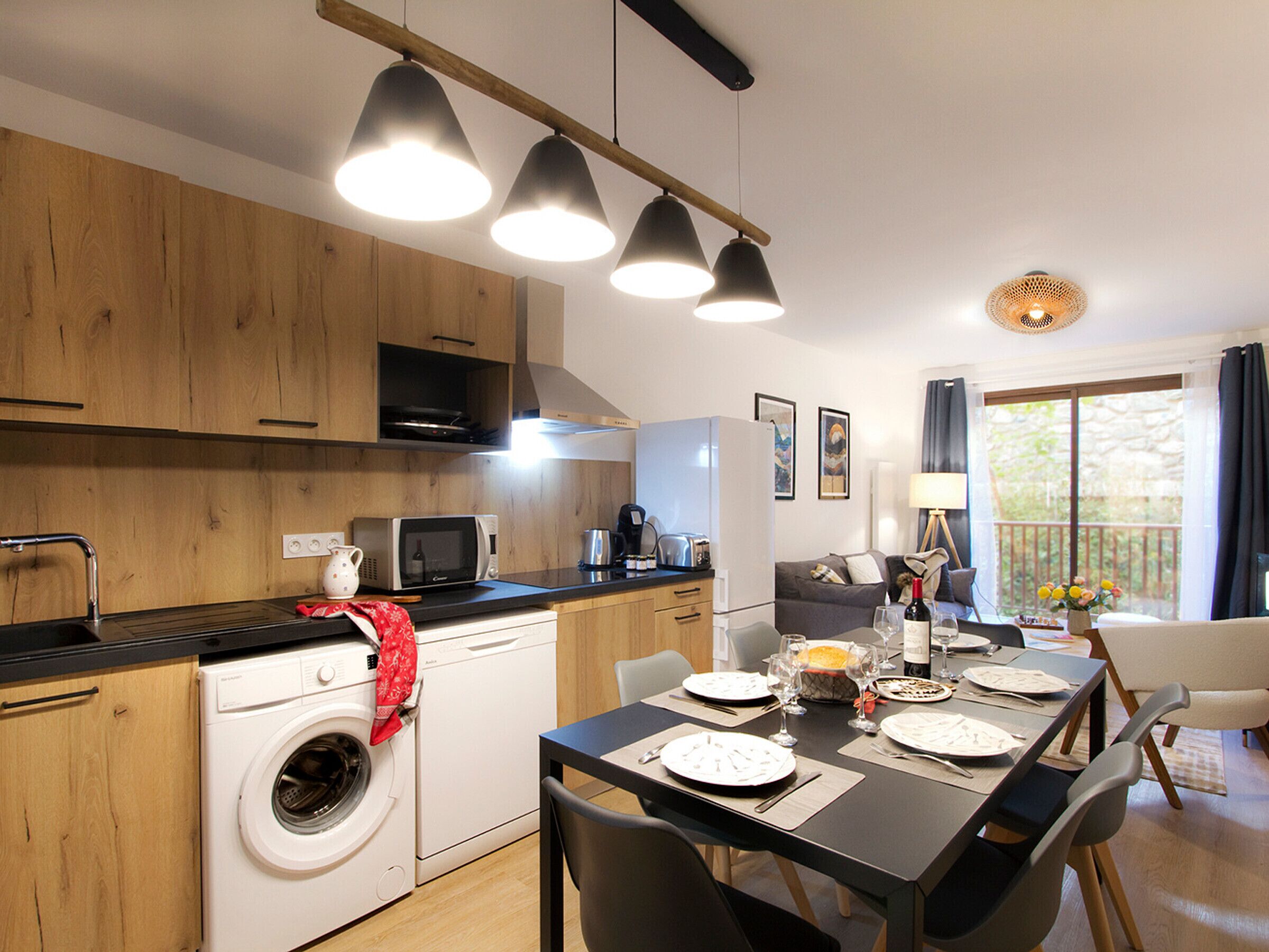 A modern kitchen with wooden cabinets, a built-in washing machine, and a dining area with a table set for four.