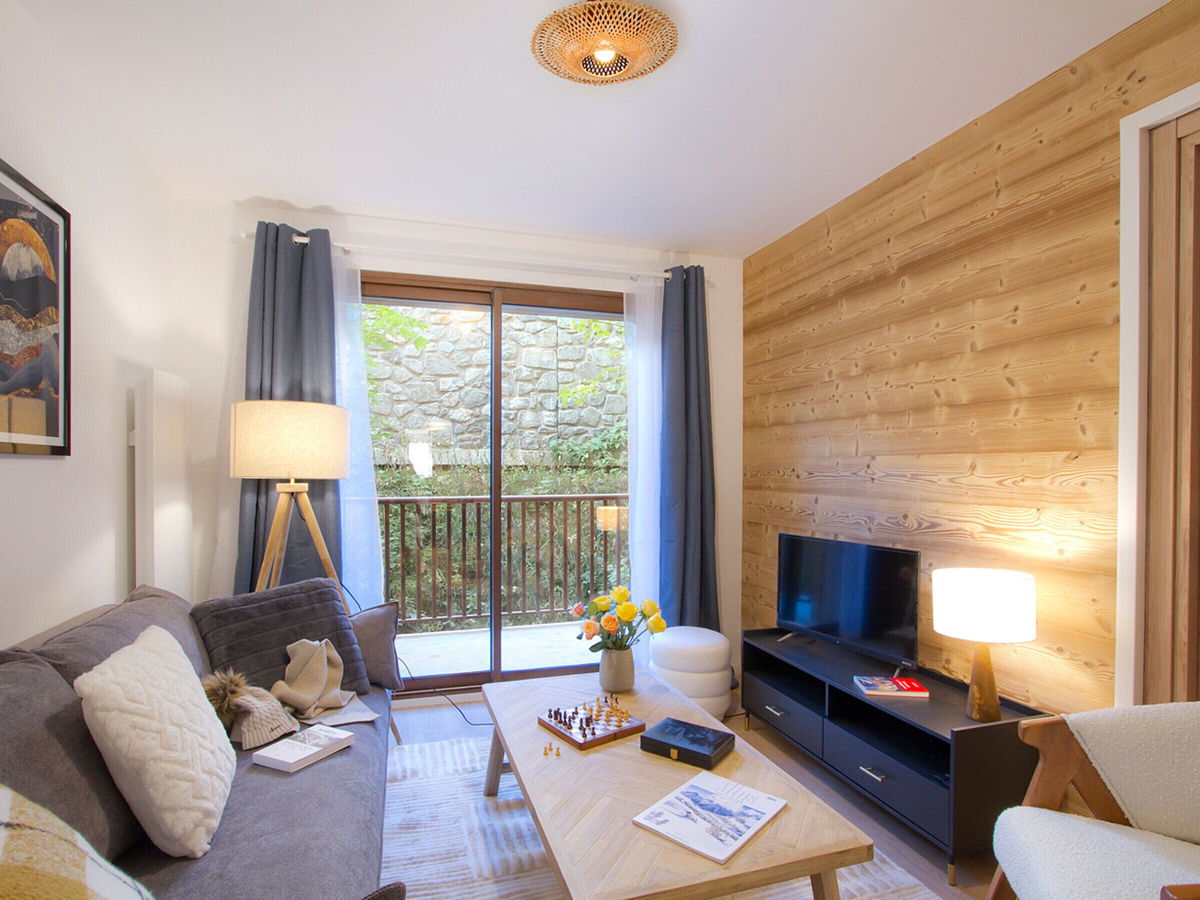 A modern living room with a sofa, coffee table, TV, and a stone wall view.