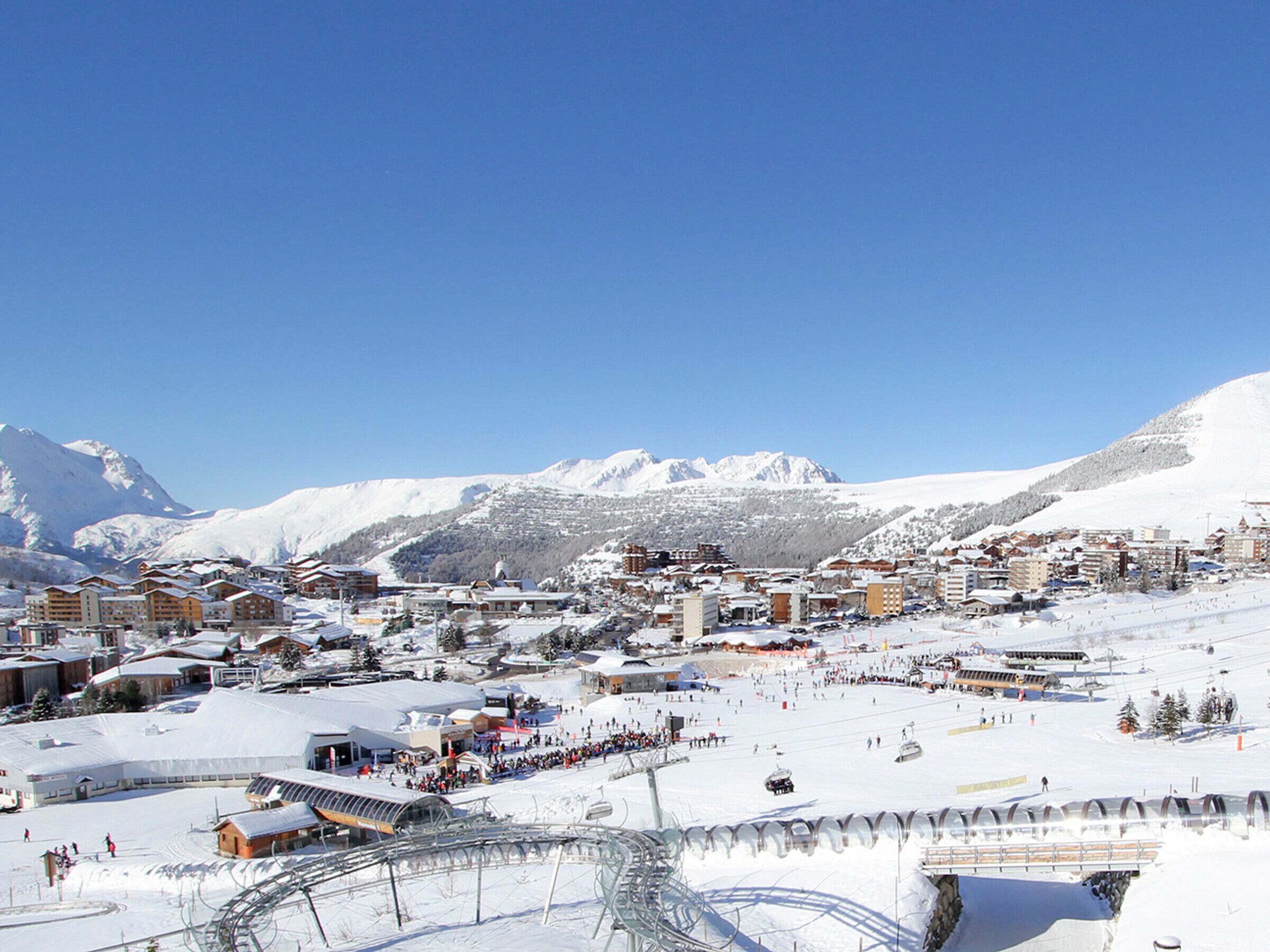 A snow-covered mountain town with buildings, ski slopes, and a clear blue sky.