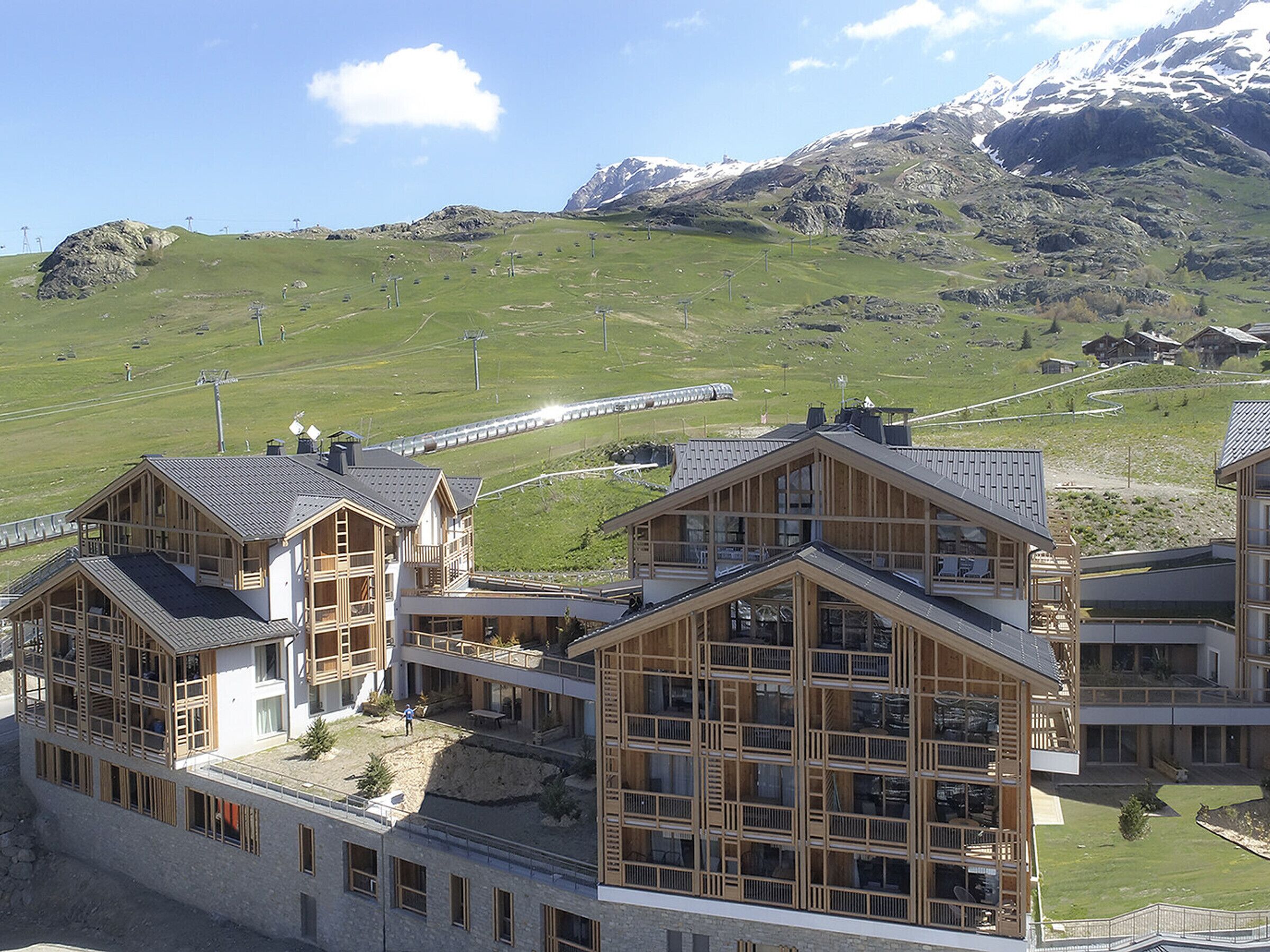 Un hotel moderno con diversi piani e ampie finestre, con vista su dolci colline e una catena montuosa.