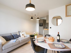A modern living room with a sofa, dining table set for two, and a kitchen in the background. - Bright apartment with parking - 4 guests (Huez)