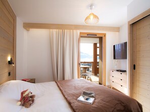 A bedroom with a bed, a television, a wooden dresser, and a view of a balcony. - Spacious apartment ski-in/ski-out - 8 guests (Huez)