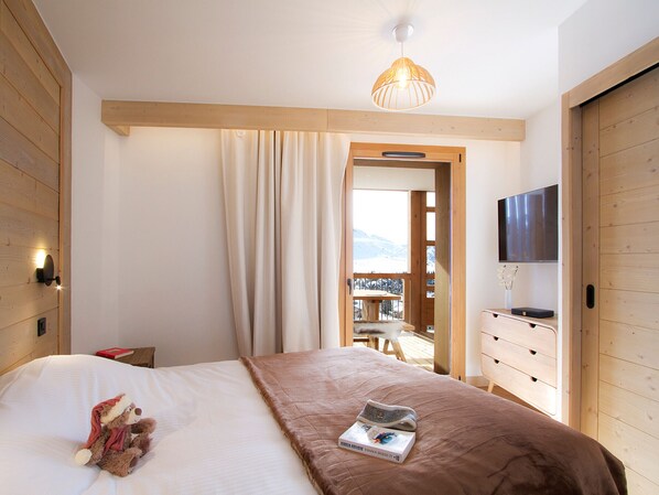 A bedroom with a bed, a television, a wooden dresser, and a view of a balcony. - Spacious apartment ski-in/ski-out - 8 guests (Huez)