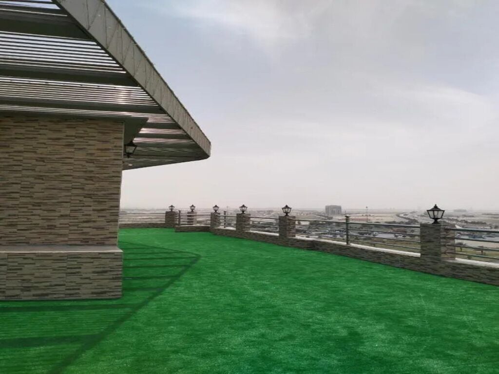 Una terraza en la azotea con césped artificial verde, un muro de piedra y una barandilla de metal.