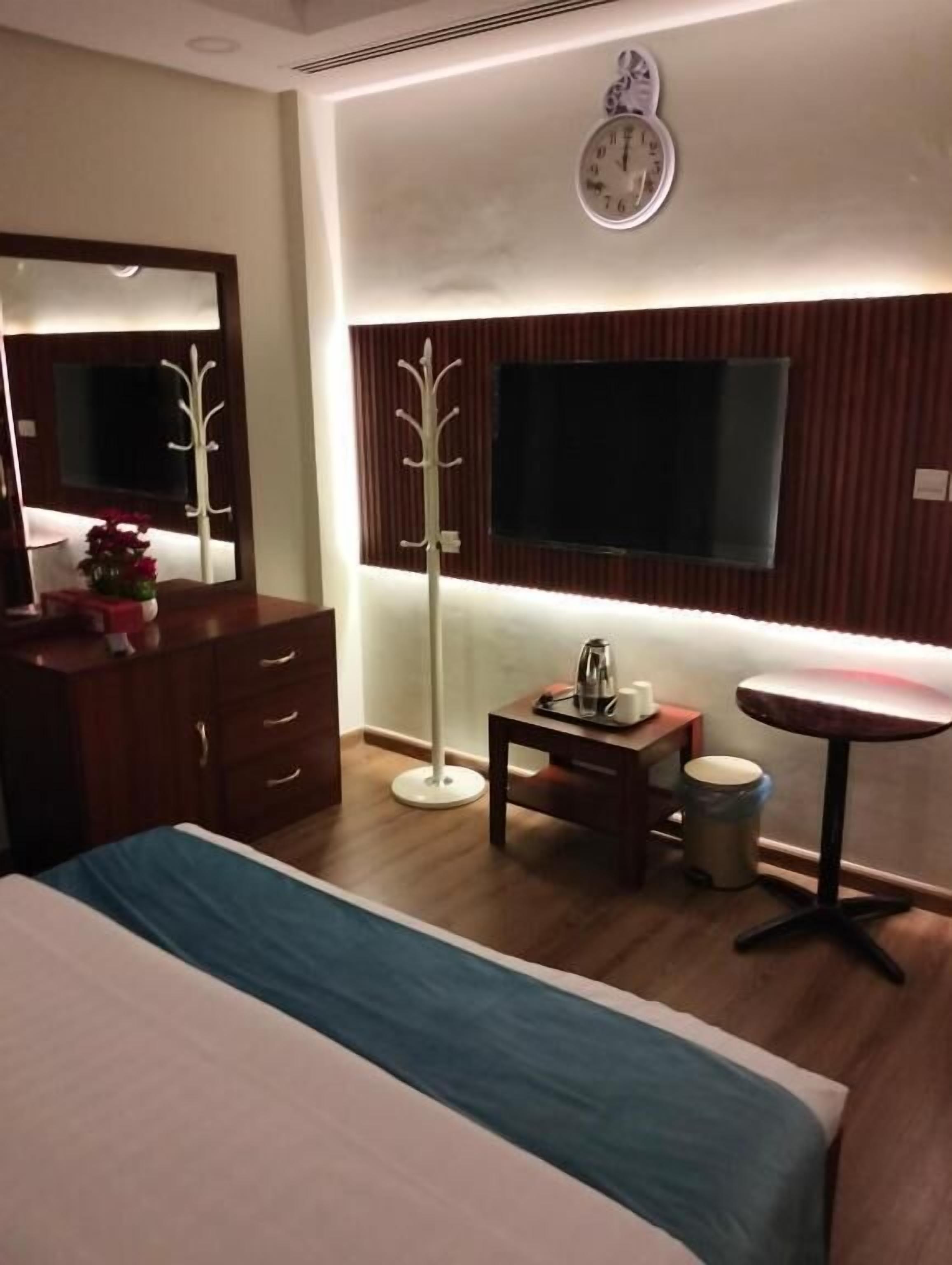 Una habitación de hotel con cama, espejo, perchero, televisor, una mesita y una mesa redonda.