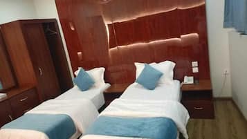 Habitación de hotel con dos camas individuales, un armario de madera y una mesita de noche con teléfono.