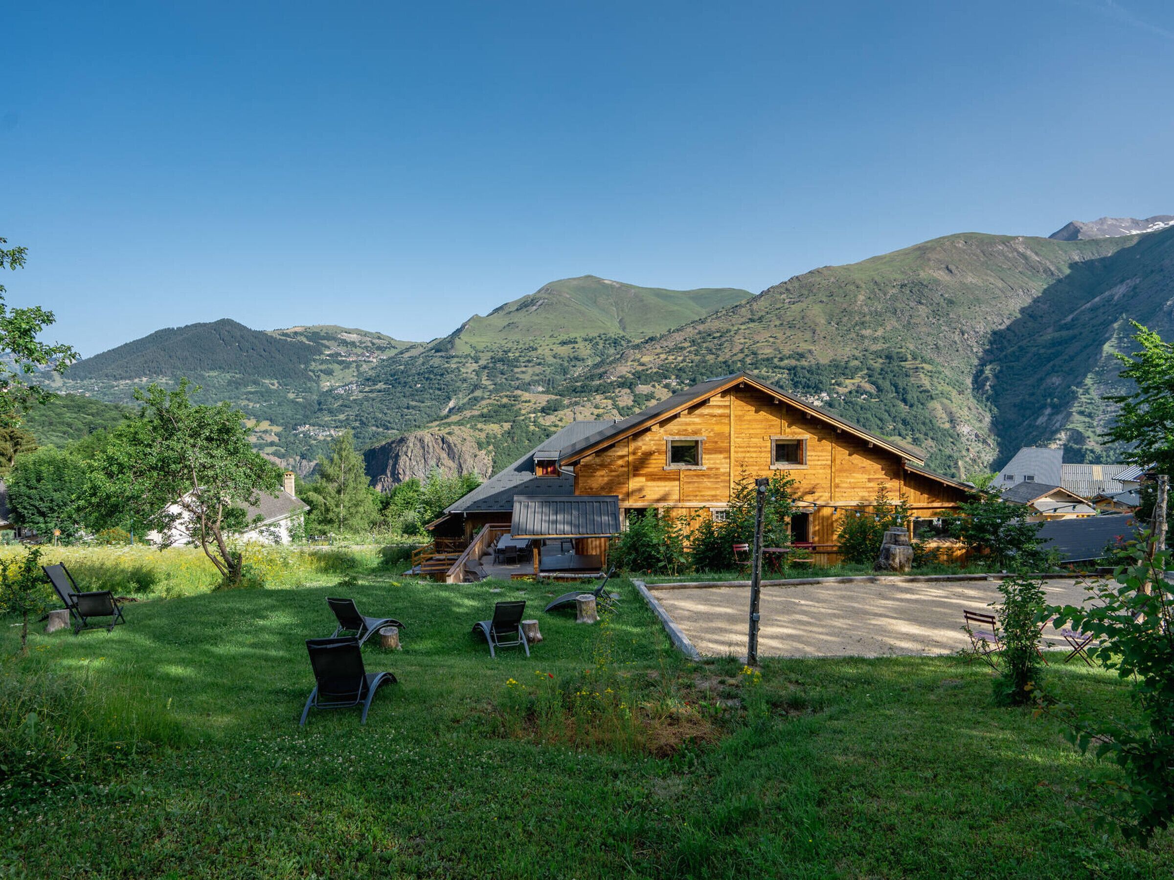 Eine Holzhütte mit einer Terrasse und Sitzgelegenheiten im Freien, umgeben von üppiger Vegetation und Bergen.