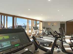 Een sportschool met loopbanden en fitnessapparatuur, grote ramen met uitzicht op een berg, en een modern interieur.