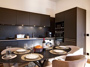 A modern kitchen with dark cabinetry, a dining table set for six with plates, cutlery, and glasses, and a wine bottle. - Top-floor apartment, piste view - 6 guests (Huez)