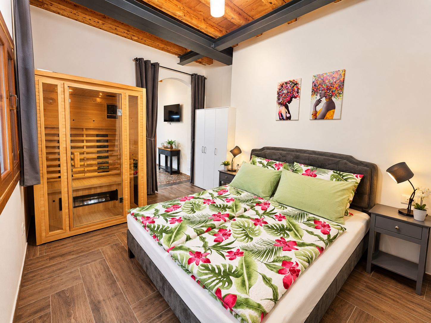 A bedroom with a bed, a wardrobe, a television, and artwork on the wall.