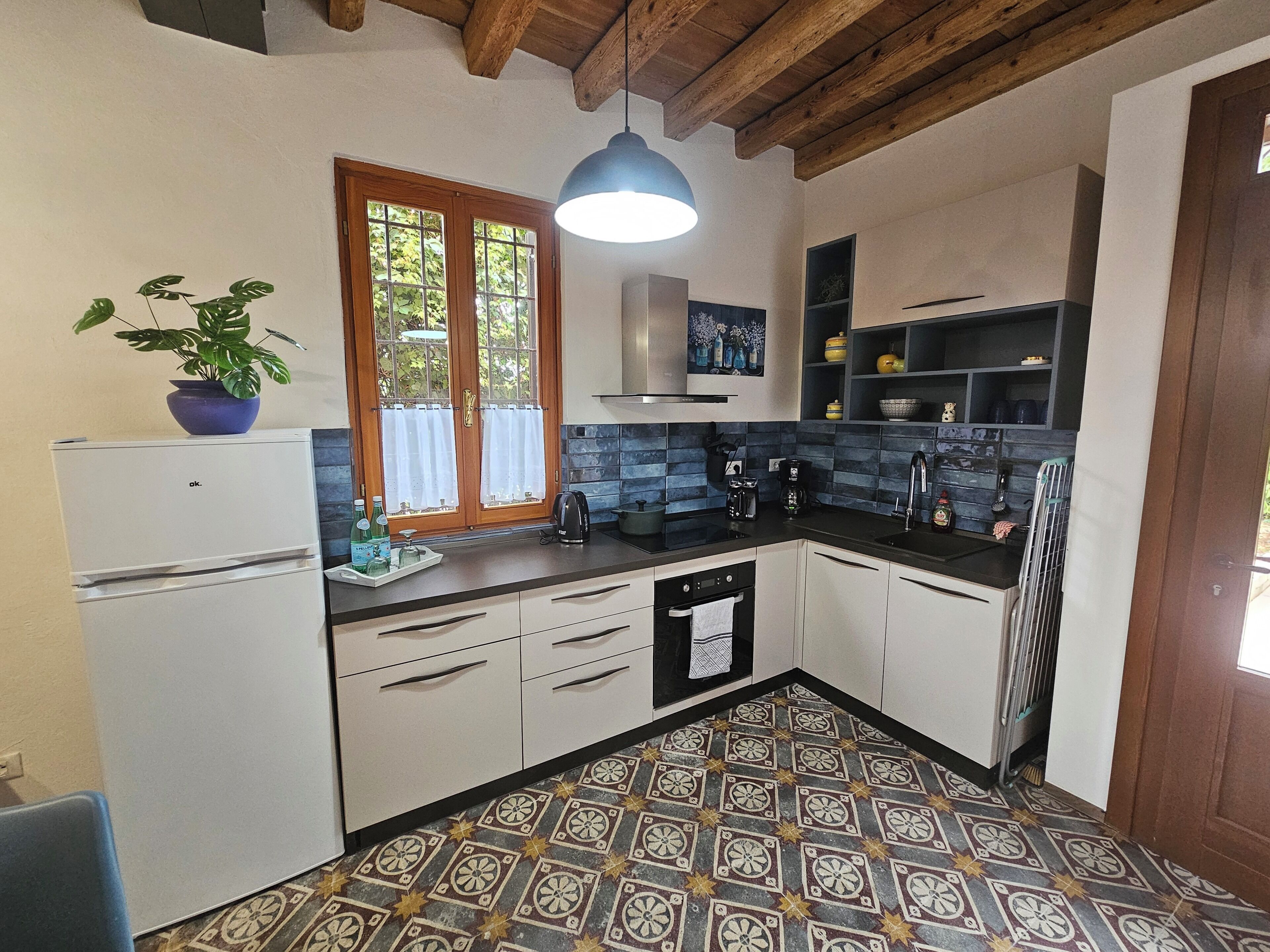 A compact kitchen with a refrigerator, a sink, a stove, and a window with curtains.