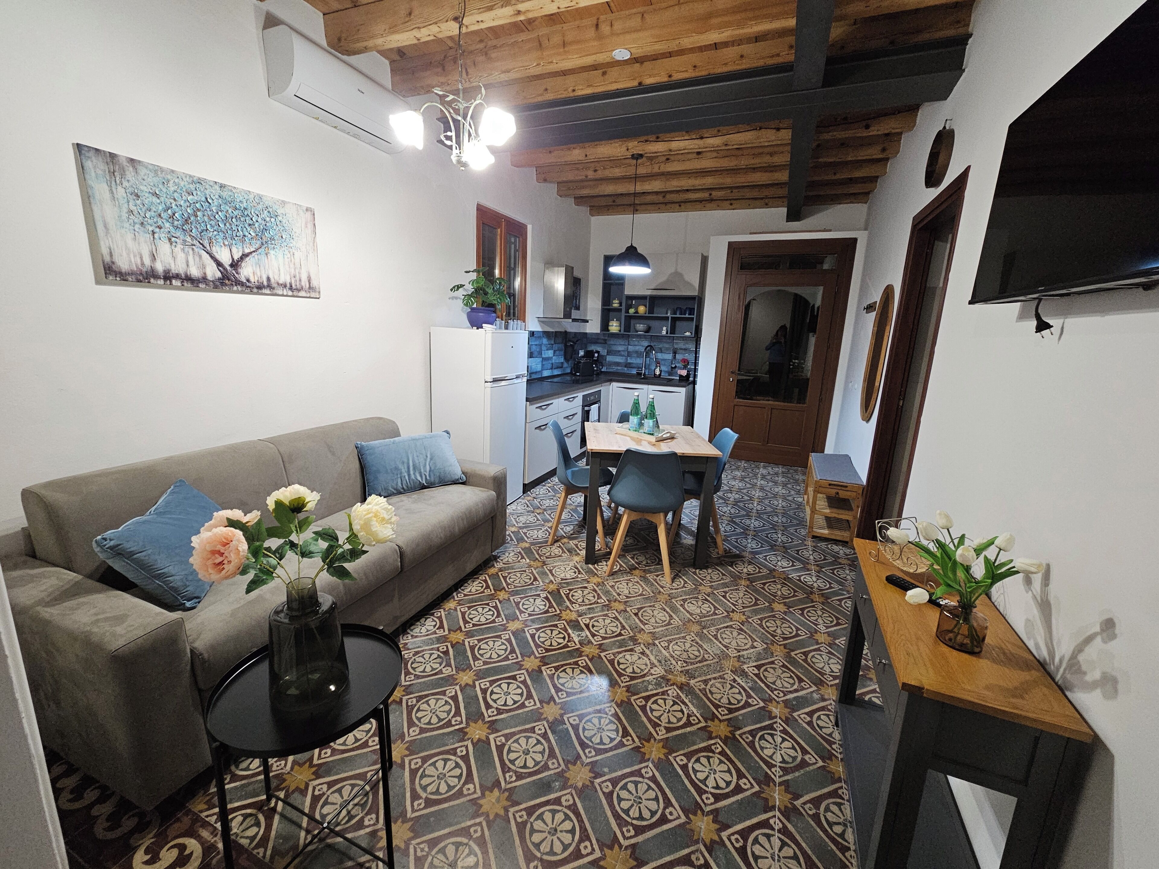 Un salon comprenant un canapé, une table à manger avec des chaises, un coin cuisine et un téléviseur fixé au mur.