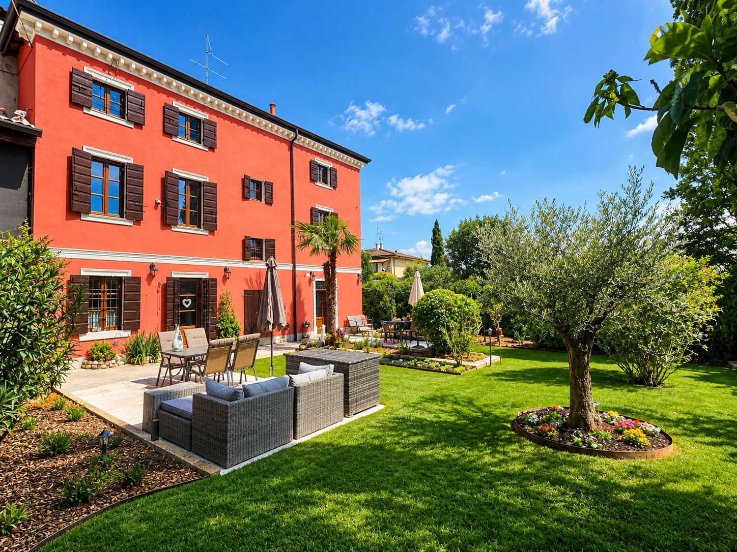 A red building with a patio area, outdoor furniture, and a well-maintained garden.