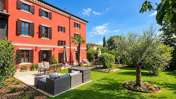 A red building with a patio area, outdoor furniture, and a well-maintained garden.