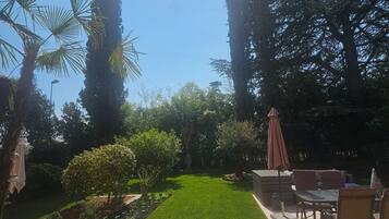 Ein gepflegter Garten mit Rasenflächen, verschiedenen Pflanzen und einer Sitzgelegenheit mit Tischen und Stühlen.
