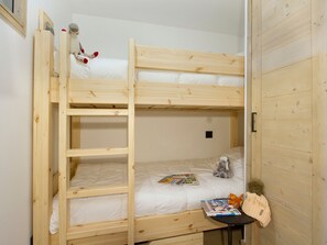 Ein Stockbett mit einer Leiter, ein kleiner Tisch mit Büchern und einem Hut, und ein Stofftier auf dem oberen Bett.