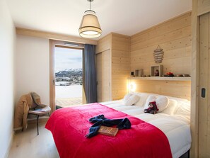 Ein Hotelzimmer mit einem großen Bett, einem Sessel, einer Holzwand und Blick auf eine verschneite Landschaft.