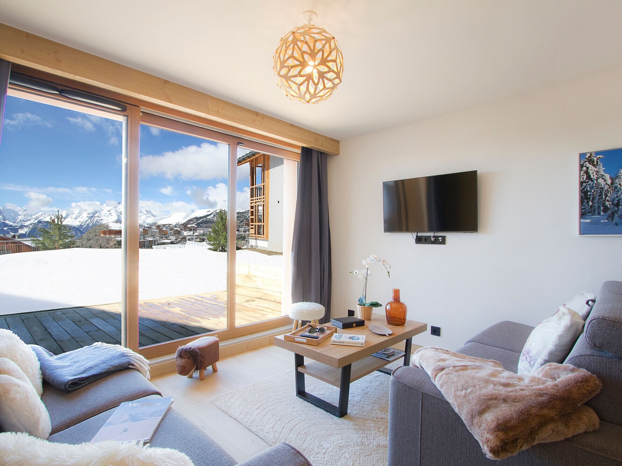 Uma sala de estar moderna com uma grande porta de vidro deslizante que dá para uma área externa coberta de neve, uma TV de tela plana na parede e um sofá aconchegante com um cobertor fofo.